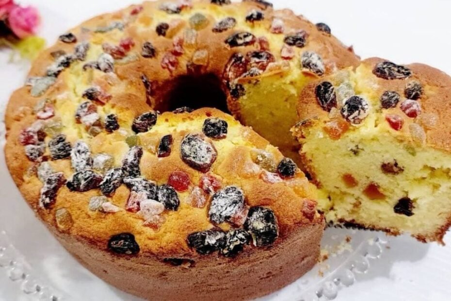 Bolo panetone na forma, dourado e decorado com frutas cristalizadas, servido em prato natalino.